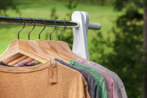 Organic clothes, t shirts hanging on wooden hangers with green forest, nature in background.